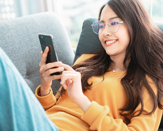 Young woman laying on couch and scrolling on her phone