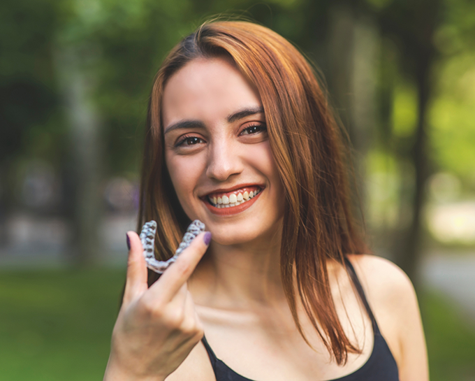 Young woman smiling and holding a clear aligner