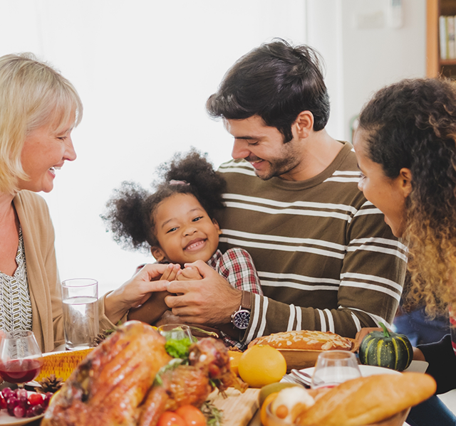 Three generations of a family laughing at Thanksgiving dinner table