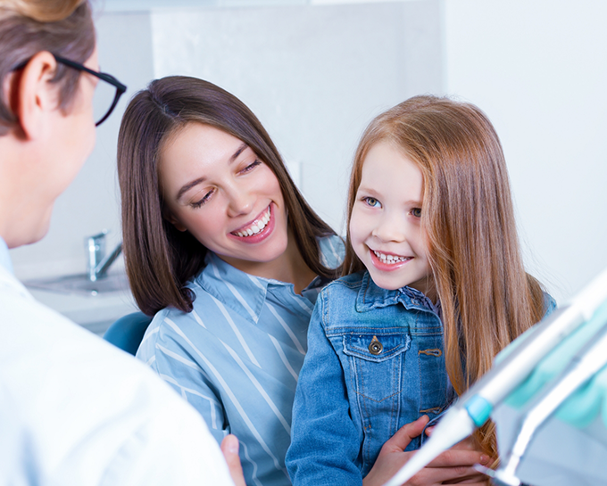 Young girl sitting in her mothers lap while talking to orthodontist