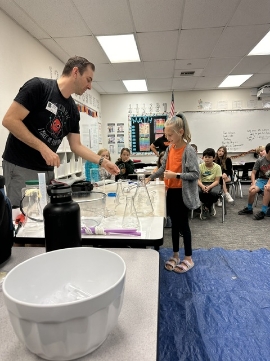 Doctor Larson talking to a young girl during a science presentation at a table with beakers and glasses