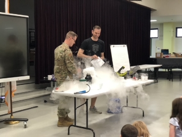 Doctor Larson and another adult at table with lab experiment creating vapor